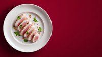 Sliced pork tenderloin with herbs on white plate against burgundy background for culinary presentations and restaurant menus.