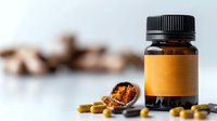 Amber glass bottle with blank orange label and natural supplement capsules scattered on white surface, golden turmeric powder in spoon, wellness concept.