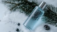 Luxurious blue cosmetic bottle with bubbles on snowy background with pine branches and berries, perfect for winter skincare advertising.