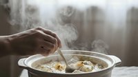 Hand stirring hot homemade soup with steam rising from pot, comfort food cooking in kitchen for warming meal preparation and culinary dining experience.