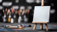 Empty white canvas on wooden mini easel with scattered art supplies and paintbrushes in dark studio setting, creative workspace atmosphere with bokeh background.