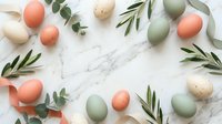 Easter eggs in pastel colors with eucalyptus and olive branches arranged in circle frame on white marble background for spring holiday celebration.