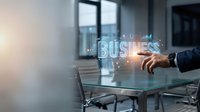 Professional businessman hand touching glowing holographic business text in modern office conference room with glass table and city view windows.