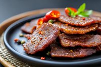 Grilled spicy sausage slices with herbs and chili peppers on dark plate, ready to serve as appetizer or main course for restaurant menu and food photography.