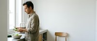 Young Caucasian man in beige shirt preparing healthy meal in modern minimalist kitchen with natural lighting for cooking and lifestyle content.