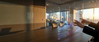 Businessman interacting with holographic digital interface on conference table in modern office space with glass partitions and city skyline view for corporate technology solutions.