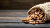 Mixed dried fruits and nuts spilling from rustic burlap sack onto dark wooden surface, creating natural composition with warm golden tones and rich textures.
