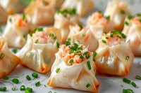 Steamed shrimp dumplings garnished with fresh chopped chives on white plate, close up view of Asian dim sum appetizers with translucent wonton wrappers.