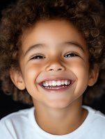 Joyful young child with curly afro hair and bright genuine smile wearing white t-shirt against dark background, expressing pure happiness and innocence.