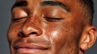 Close-up portrait of young African American man with freckles, eyes closed, showing natural skin texture and peaceful expression.