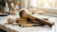 Professional makeup brushes with wooden handles and gold ferrules arranged on marble surface in bright natural light for beauty and cosmetics applications.