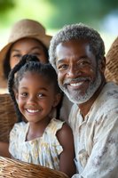 African American grandfather with gray beard smiling warmly with granddaughter outdoors, showing loving family bond and multi-generational connection in natural setting.