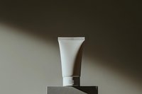 White cosmetic tube on gray pedestal against dark background with dramatic lighting and shadow. Minimalist product photography for beauty and skincare advertising.