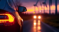 Car tail light glowing on dark rural road at sunset with wind turbines silhouetted against dramatic orange sky, approaching vehicle headlights in distance.