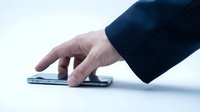 Male hand in dark business sleeve touching smartphone screen on white surface, representing mobile technology interaction and digital communication.
