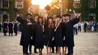 Group of diverse young graduates in caps and gowns celebrating together on university campus courtyard at golden hour sunset with historic buildings.