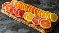 Fresh sliced citrus fruits arranged on wooden board including orange, grapefruit and lemon circles creating colorful gradient pattern on dark background.