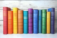 Row of colorful hardcover books arranged in rainbow spectrum order standing against white wooden background, creating vibrant educational display.