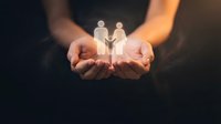 Cupped hands holding glowing paper cutout figures representing family protection, care and support concepts for insurance and social services.