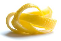 Fresh spiral lemon peel with textured yellow rind isolated on white background, showing citrus zest detail for culinary and cocktail garnish uses.