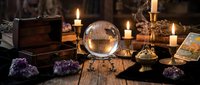 Mystical fortune telling setup with crystal ball, tarot cards, amethyst crystals and burning candles creating atmospheric divination scene for spiritual practices.