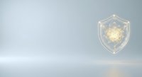Glowing shield with golden light particles floating inside transparent geometric protection symbol on neutral background for security concepts.