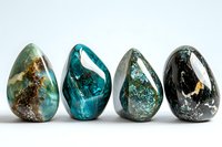 Polished natural gemstones in teardrop shapes featuring turquoise, blue apatite, and black minerals arranged in row on white background, showing unique patterns and textures.