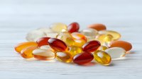Colorful vitamin and fish oil capsules scattered on white wooden background, nutritional supplements in orange, yellow and clear gel pills.