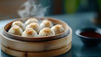 Steaming hot soup dumplings in traditional bamboo steamer with dipping sauce on dark background, fresh Asian cuisine preparation.