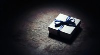 White gift box with black ribbon bow on dark textured surface, suitable for holiday, celebration, and luxury product packaging designs.