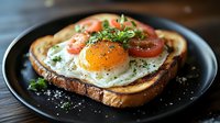 Sunny side up egg on toasted bread garnished with fresh tomato slices, herbs and black pepper served on dark plate against wooden background. Great for breakfast menu.