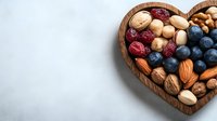 Heart shaped wooden bowl filled with assorted nuts, dried cranberries, blueberries, and pistachios on light background. Healthy snack concept for Valentine's day.