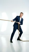 Determined businessman in navy suit pulling rope in tug of war competition showing leadership and teamwork on white studio background.