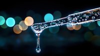Crystal clear water droplet forming at edge of transparent glass surface with colorful bokeh lights creating magical atmosphere for wellness concepts.