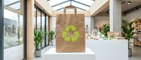 Brown paper shopping bag with green recycling symbol displayed in modern eco-friendly retail store interior with natural lighting and plants.