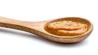 Creamy peanut butter in wooden spoon isolated on white background, natural organic spread showing smooth texture and golden brown color.