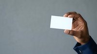 Man with dark skin tone holding blank white business card against gray background for corporate branding and marketing purposes.