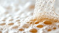 Macro shot of golden beer foam with bubbles and froth creating abstract pattern on light background, soft focus highlighting delicate texture and depth.