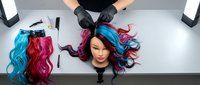 Stylist hands in black gloves arranging colorful synthetic hair extensions in blue, pink, and magenta shades on white workspace for salon or wig design work.