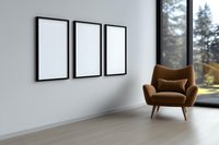 Modern minimalist living room interior with three blank white frames on wall, brown retro armchair near panoramic window with forest view.