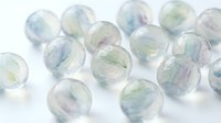 Translucent spheres with soft pastel swirls of blue, green, and purple suspended in clear resin, scattered on white surface for design, art, and creative projects.