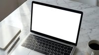 Modern laptop computer with blank white screen on marble desk workspace with coffee cup and pens for business presentations and mockup designs.