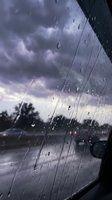 Raindrops on car window during storm with dramatic purple clouds and wet road creating moody atmospheric weather scene for transportation safety concepts.
