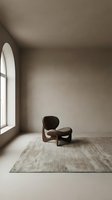 Minimalist interior space featuring a sculptural lounge chair with curved wooden frame and dark upholstery positioned on neutral area rug beside arched window. Ideal for interior design, furniture retail, and architectural visualization.