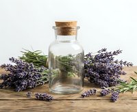 Glass bottle with cork stopper surrounded by fresh lavender and rosemary on rustic wooden table, aromatherapy and natural wellness concept.