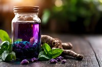 Vibrant purple butterfly pea flower tea in glass jar with fresh mint leaves and dried flowers on rustic wooden surface, natural light and bokeh background.