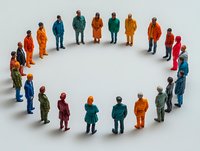 Diverse group of miniature people figures standing in circle formation on white background, representing community, teamwork and social connection concept.