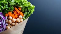 Fresh vegetables and chickpeas in brown paper bag on dark background, healthy grocery shopping concept for plant based cooking and meal preparation.