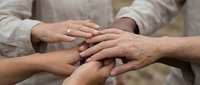 Diverse group of hands stacked together in unity gesture showing teamwork, collaboration and support in warm natural lighting for community concepts.
