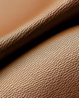 Close-up macro shot of brown leather texture showing natural grain pattern and surface details with soft shadows creating depth and dimension.